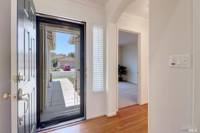 entryway featuring arched walkways, a textured wall, light wood-style flooring, ornamental molding, and baseboards