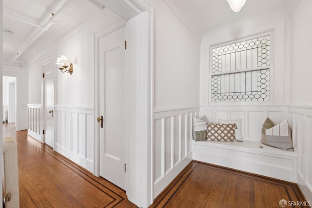 hallway with a wainscoted wall, wood finished floors, and a decorative wall