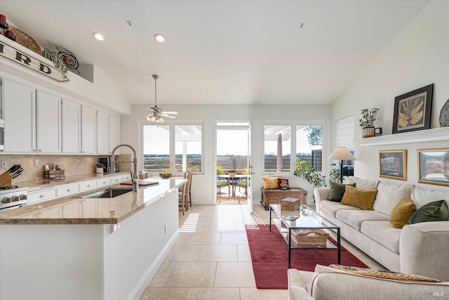 interior space featuring open floor plan, light tile patterned floors, decorative backsplash, white cabinets, and a sink