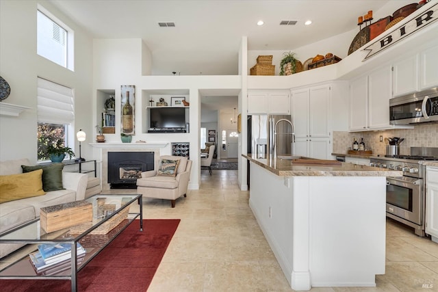 kitchen featuring visible vents, stainless steel appliances, white cabinets, a fireplace, and a towering ceiling