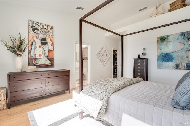 bedroom featuring visible vents, light wood-style flooring, a walk in closet, and connected bathroom