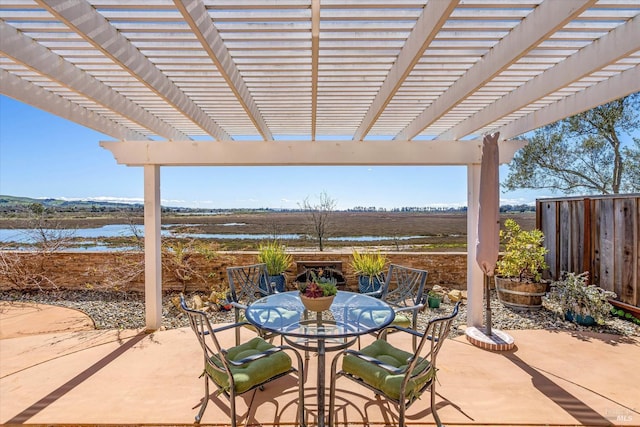 view of patio featuring a pergola, outdoor dining area, fence, and a water view