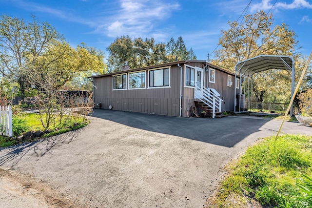 view of front of home with aphalt driveway, a carport, entry steps, and fence