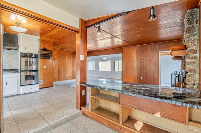 kitchen with a ceiling fan, wood ceiling, wood walls, light tile patterned flooring, and stainless steel double oven