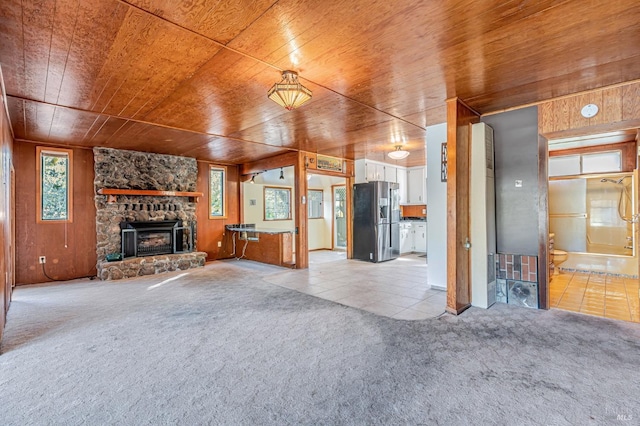 unfurnished living room with a fireplace, wooden walls, light colored carpet, and wood ceiling