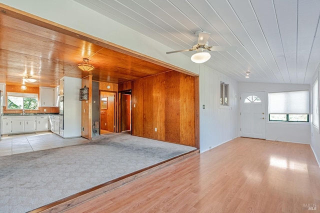 unfurnished living room featuring wooden walls, a ceiling fan, wooden ceiling, and light wood-style floors