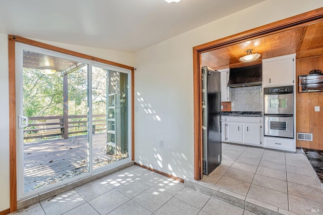 kitchen featuring freestanding refrigerator, exhaust hood, double oven, white cabinets, and light tile patterned flooring