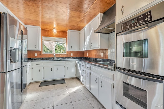 kitchen featuring light tile patterned floors, decorative backsplash, stainless steel appliances, wall chimney range hood, and a sink