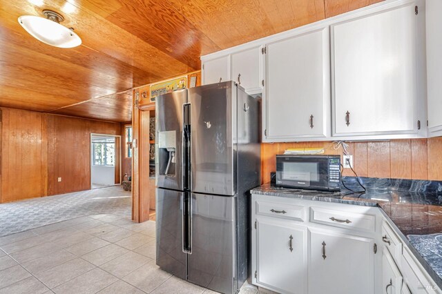 kitchen featuring black microwave, wood walls, wood ceiling, and stainless steel fridge with ice dispenser