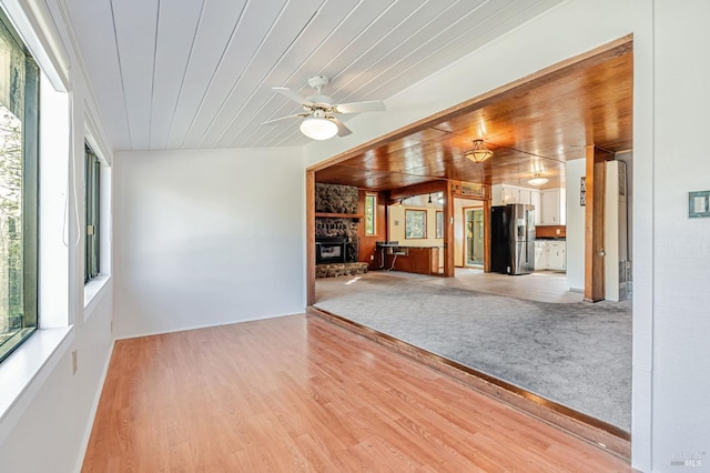 unfurnished living room featuring a ceiling fan, a wood stove, light wood finished floors, and wood ceiling
