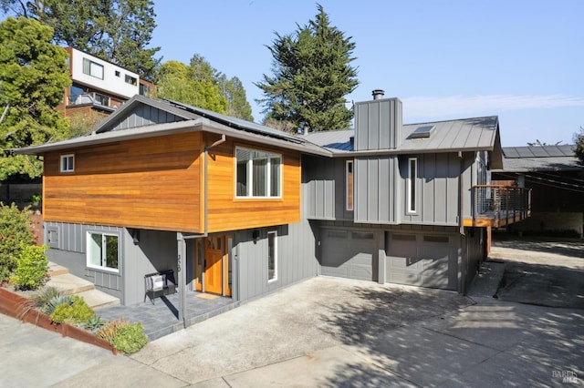 back of house with concrete driveway, a chimney, an attached garage, and solar panels