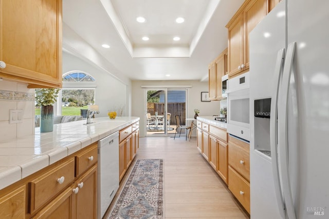 kitchen featuring a tray ceiling, tile countertops, recessed lighting, light wood-style flooring, and white appliances