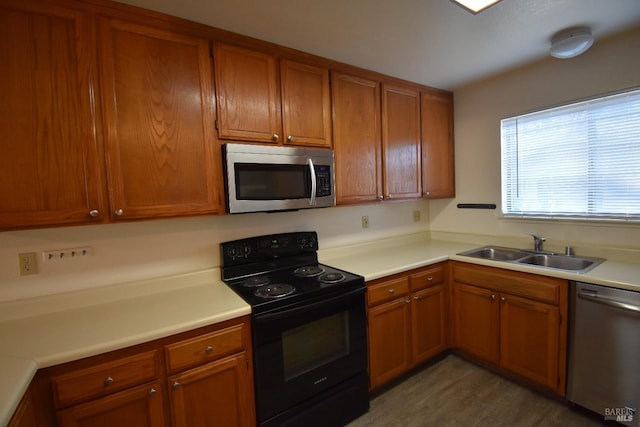 kitchen with appliances with stainless steel finishes, brown cabinets, light countertops, light wood-type flooring, and a sink