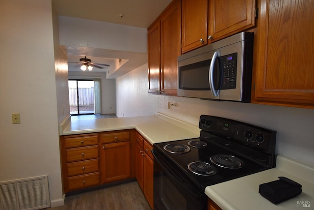 kitchen with brown cabinets, black range with electric cooktop, stainless steel microwave, and visible vents