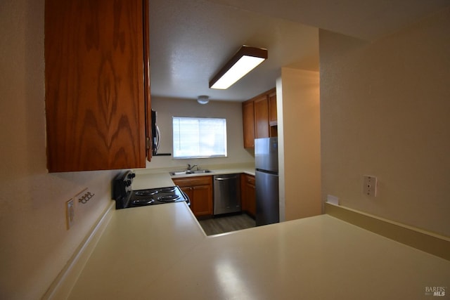 kitchen featuring brown cabinetry, appliances with stainless steel finishes, a peninsula, light countertops, and a sink