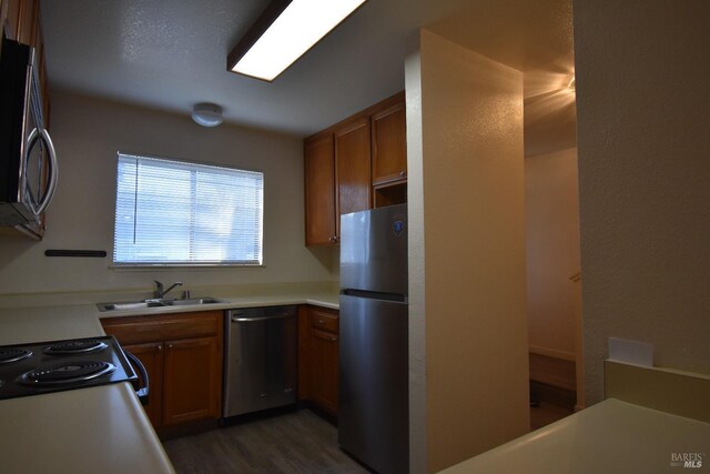 kitchen with light countertops, appliances with stainless steel finishes, brown cabinetry, a sink, and wood finished floors