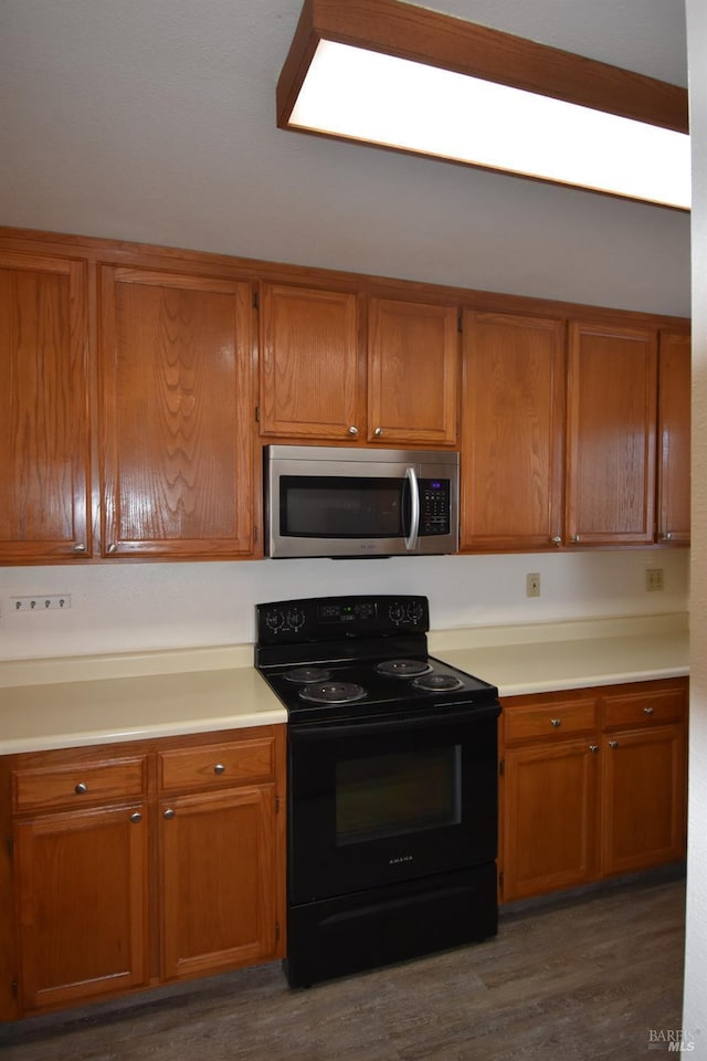 kitchen featuring black electric range, stainless steel microwave, light countertops, and wood finished floors