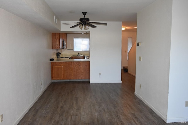 kitchen with dark wood-style floors, gas range oven, baseboards, and brown cabinetry