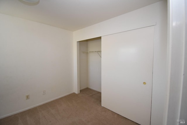 unfurnished bedroom featuring a closet, light carpet, and baseboards