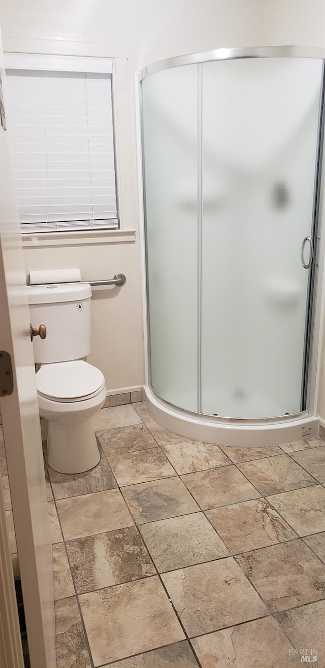 full bath featuring stone finish floor, a stall shower, toilet, and baseboards