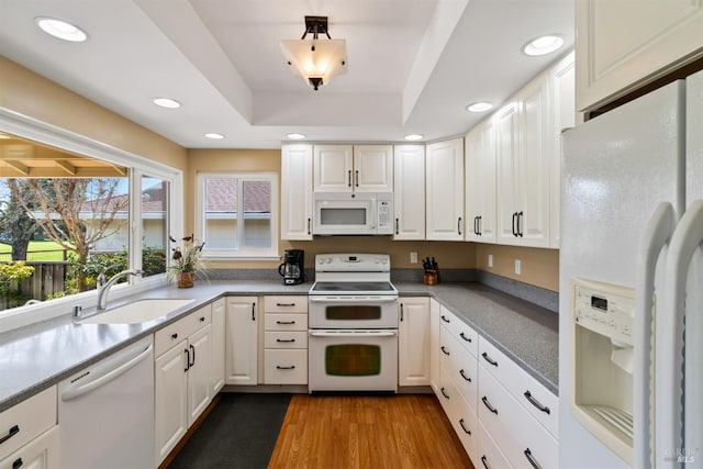 kitchen featuring a sink, wood finished floors, white appliances, white cabinets, and a raised ceiling