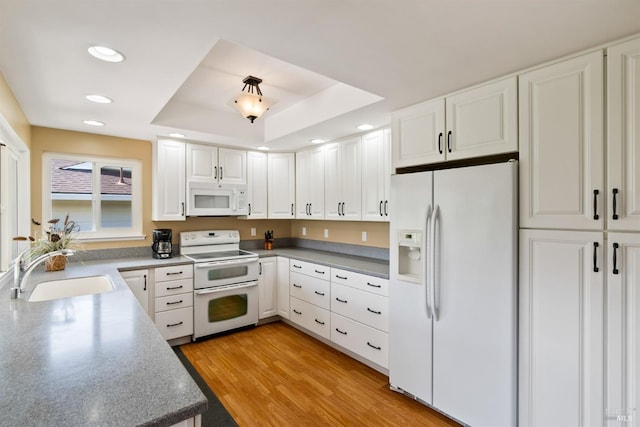 kitchen featuring light wood-style flooring, a sink, white cabinetry, white appliances, and a raised ceiling