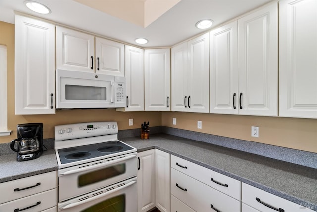 kitchen featuring dark countertops, white cabinets, and white appliances