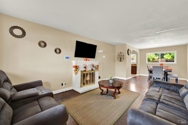 living area featuring a glass covered fireplace, dark wood-type flooring, baseboards, and arched walkways