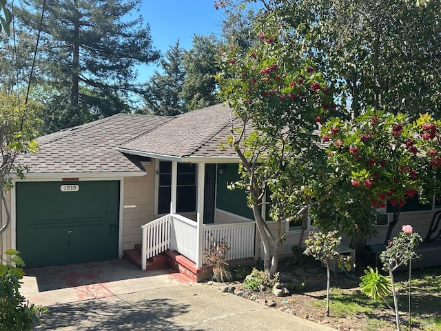 view of front of property featuring a garage, driveway, a porch, and roof with shingles