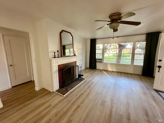 unfurnished living room featuring a ceiling fan, a brick fireplace, baseboards, and wood finished floors