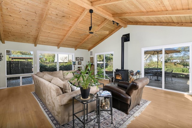 living area featuring beamed ceiling, wooden ceiling, a wood stove, and wood finished floors