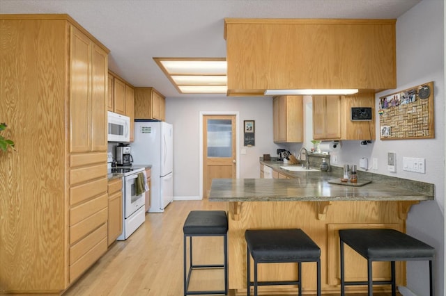 kitchen with a breakfast bar, light wood-style flooring, a sink, white appliances, and a peninsula