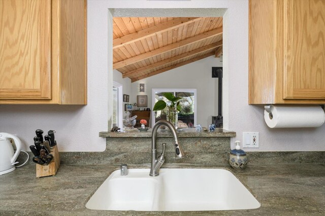 kitchen featuring dark countertops, a wood stove, vaulted ceiling with beams, a sink, and wooden ceiling