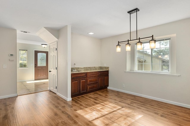 kitchen featuring visible vents, light wood finished floors, a sink, and baseboards