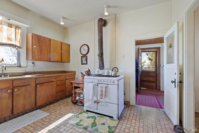 kitchen featuring white gas stove, a sink, light countertops, brown cabinets, and light floors
