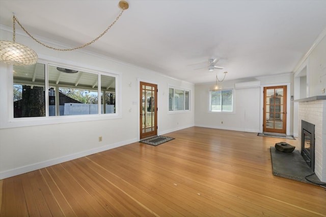 unfurnished living room with a fireplace, light wood-style floors, a wall mounted air conditioner, and ceiling fan