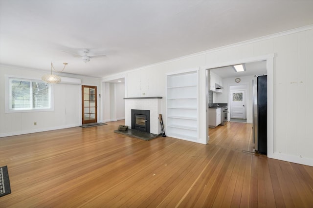 unfurnished living room with a ceiling fan, a fireplace, a wall unit AC, and light wood-style flooring