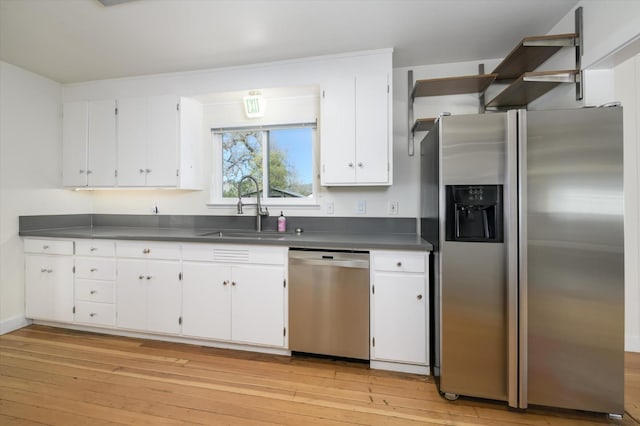 kitchen featuring dark countertops, a sink, light wood finished floors, white cabinets, and appliances with stainless steel finishes