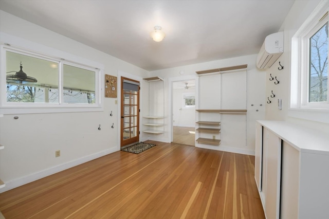 unfurnished dining area with light wood-type flooring, baseboards, and a wall unit AC