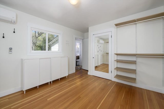 unfurnished bedroom with baseboards, light wood-style flooring, and a wall unit AC