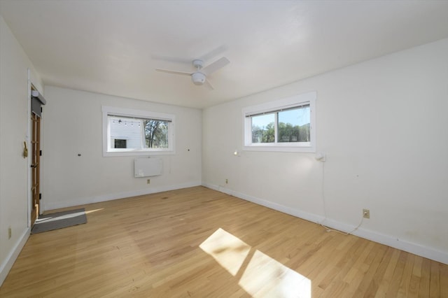 empty room featuring light wood finished floors, a ceiling fan, baseboards, and a wealth of natural light