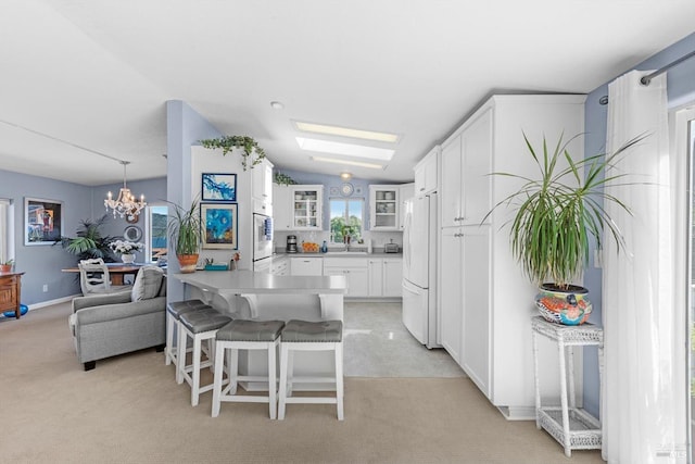 kitchen with a kitchen bar, white cabinetry, freestanding refrigerator, a peninsula, and glass insert cabinets