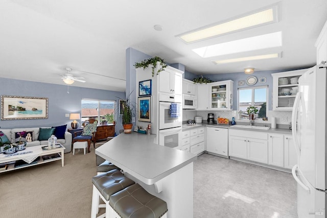 kitchen with a sink, plenty of natural light, open floor plan, white appliances, and a peninsula