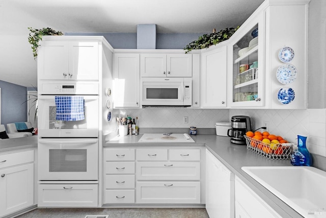 kitchen with white appliances, a sink, glass insert cabinets, white cabinetry, and tasteful backsplash