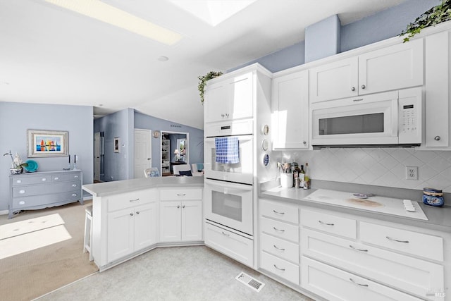 kitchen with white appliances, white cabinetry, a peninsula, and light countertops