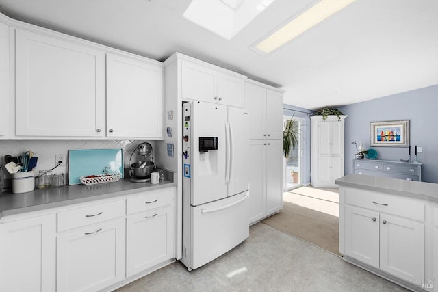 kitchen with a skylight, light countertops, white fridge with ice dispenser, white cabinetry, and tasteful backsplash