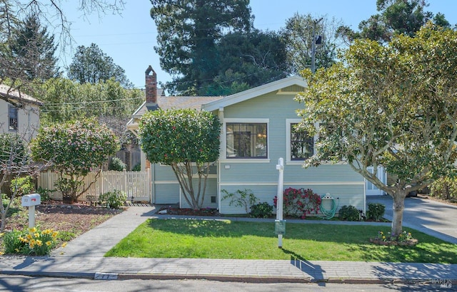 view of front facade featuring a chimney, a front yard, and fence