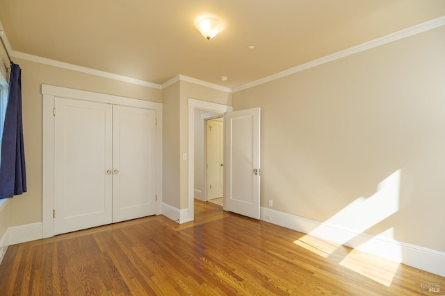 unfurnished bedroom featuring baseboards, a closet, wood finished floors, and crown molding