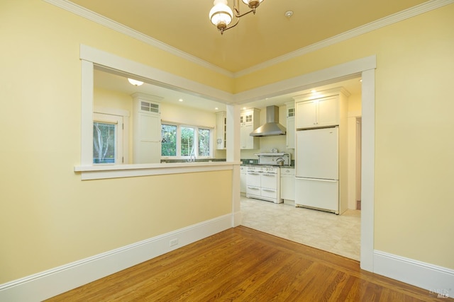 kitchen featuring light wood-style flooring, glass insert cabinets, ornamental molding, wall chimney range hood, and white appliances