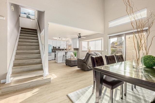 dining room with stairway, a ceiling fan, light wood-style floors, baseboards, and a high ceiling